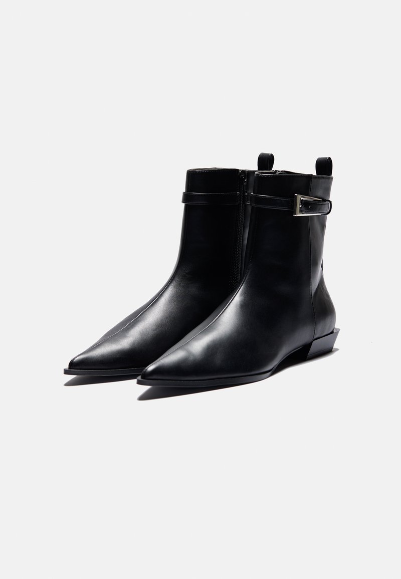 Zwarte leren enkellaarsjes met een spitse neus, zijrits en een bandje met een zilveren gesp. Gladde textuur en hak van lage hoogte.