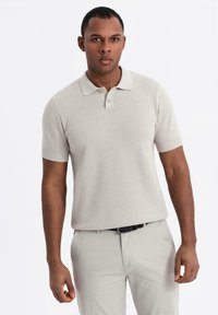 Ljusgrå kortärmad polo med ett strukturerat stickat mönster, som har en klassisk krage och två knappar. Bärs med ljusa byxor.