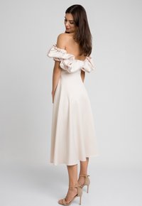 Sukienka midi bez ramiączek w odcieniu blush z bufiastymi rękawami i gładkiego materiału; ma dopasowaną górę i rozkloszowany dół, zestawiona z cielistymi szpilkami.