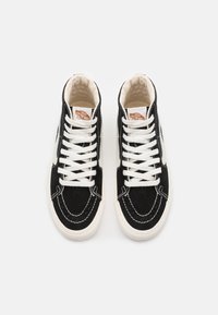 Zapatillas altas de ante negro con suelas de goma blanca, costuras blancas en contraste y cordones blancos. Presenta una etiqueta con el logo en la lengüeta.