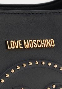Fekete műbőr táska arany tónusú "LOVE MOSCHINO" logóval és lekerekített tüskékkel a dizájn mentén. Simaság és strukturált forma jellemzi.