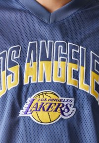Mėlynas tinklinis krepšinio marškinėliai su užrašu "LOS ANGELES" geltonomis ir baltomis raidėmis, su purpuriniu ir geltonu siuvinėtu Los Andželo "Lakers" logotipu.
