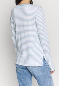 Top a maniche lunghe a righe in azzurro chiaro e bianco, con collo rotondo, fessure laterali e tessuto morbido, abbinato a jeans in denim azzurro chiaro.