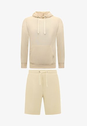 Beige hoodie met een voorzak en verstelbare trekkoorden, gecombineerd met bijpassende shorts met een elastische tailleband en trekkoord.