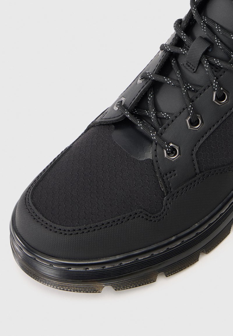 Black athletic shoe with a textured mesh upper, reinforced synthetic toe, and metallic eyelets. Features a cushioned black sole with treads.