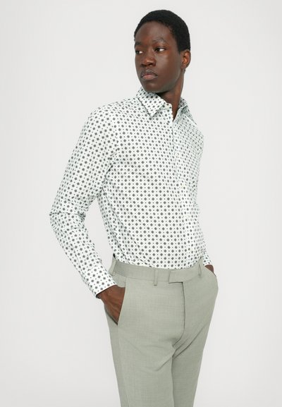White shirt with black geometric patterns, long sleeves, button-down collar, paired with light grey tailored pants. Smooth fabric texture.