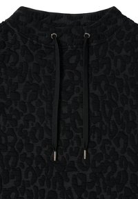 Musta huppari, jossa on teksturoitu leopardikuvio, metallisilla päillä varustetut kiristysnauhat ja resorinen kaulus.