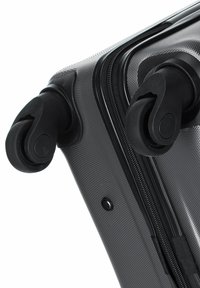 Valigia rigida nera con superficie testurizzata, dotata di due ruote girevoli nere e una cerniera lungo un lato. Design compatto e funzionale.