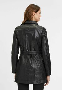 Zwarte leren jas met riem, voorzien van een aangesloten ontwerp, zichtbare stiksels en een gladde textuur. Heeft een kraag en lange mouwen.