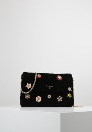 Schwarze gesteppte Handtasche mit goldener Kettenriemen, verziert mit bunten Blumen- und sternförmigen Applikationen, auf weißer Oberfläche präsentiert.
