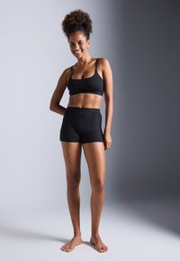 Svart sports-bh med tynne stropper og sømløst design, parret med høyt midje svarte shorts. Glatt tekstur og tettsittende stil.