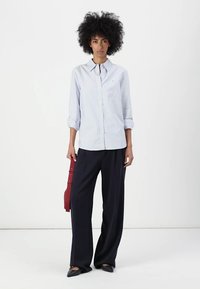 Modra in bela prugasta srajca s gumbi, z zavihki na rokavih, v kombinaciji z širokimi črnimi hlačami in rdečo torbico. Gladek material z rahlo teksturo.