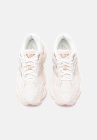Hvite sneakers med teksturert mesh og semsket overdel, med en lys rosa aksent og reflekterende detaljer på sidene. Klassisk snøringsdesign.
