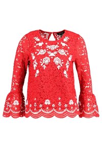 Top in pizzo rosso con maniche lunghe a campana, caratterizzato da ricami floreali bianchi e dettaglio a merletto sul bordo. Chiusura a chiave sul retro del collo.