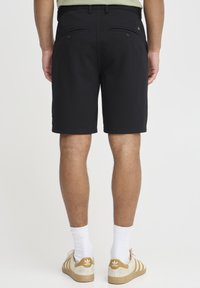 Black shorts made from a smooth fabric, featuring two back pockets with button closures, and a clean, tailored cut at knee length.
