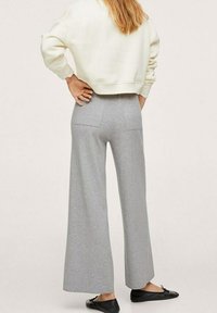 Pantaloni a gamba larga grigio chiaro in tessuto morbido, con due tasche posteriori. Abbinati a una felpa bianca corta e scarpe nere.