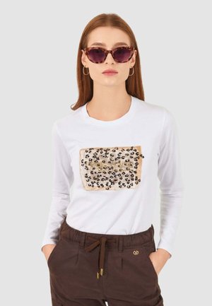 T-shirt bianca a maniche lunghe con una grafica a motivo leopardato beige e nero con dettagli dorati sul davanti. Materiale in cotone.