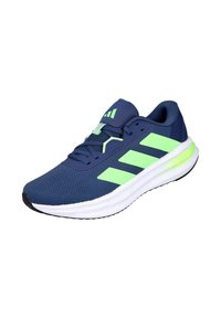 Zapatilla deportiva azul marino con rayas, cordones y detalles en la suela de color verde neón, con una entresuela blanca acolchada y suela exterior negra.