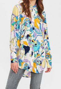 Camisa de botones hecha de un tejido ligero, con un patrón abstracto colorido en azules, amarillos y morados; mangas largas y dobladillo curvado.