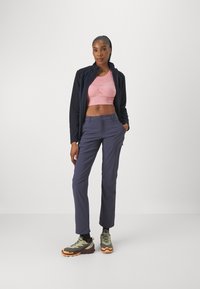 Conjunto deportivo que incluye una camiseta corta rosa, pantalones azul marino y zapatillas de senderismo verde-negro con detalles en naranja. Texturas suaves y diseño aerodinámico.