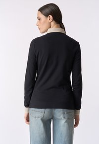 Maglietta nera a maniche lunghe con colletto beige a contrasto, tessuto morbido, design aderente e dettaglio della cucitura posteriore, abbinata a jeans blu chiaro.