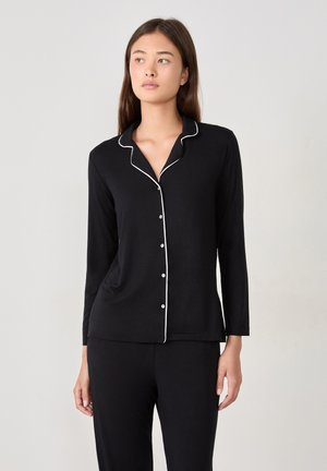 Haut de pyjama noir à manches longues avec des passepoils blancs, doté d'un col à revers et d'une fermeture boutonnée à l'avant. Tissu doux avec une coupe décontractée.