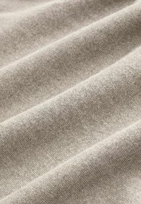 Beige szövet, puha, texturált felülettel, finom redőkkel és árnyalatbeli, valamint vastagságbeli apró eltérésekkel.