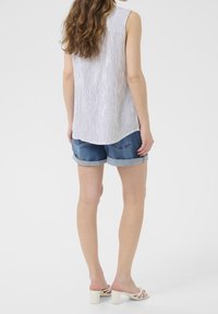 Blusa sin mangas de rayas claras con dobladillo redondeado, combinada con pantalones cortos de mezclilla doblados. La modelo lleva sandalias de tacón cuadrado blancas.