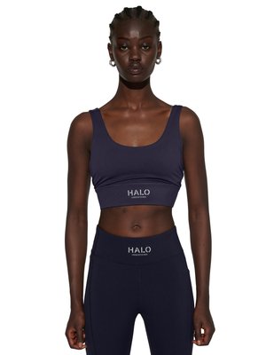 Kvinde med flettet hår iført marineblå sports-bh og matchende leggings med "HALO" logo på begge beklædningsgenstande, står mod hvid baggrund.
