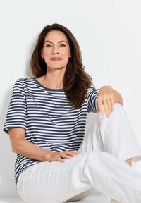 Marineblauw en witte gestreepte T-shirt met een ronde halslijn en korte mouwen, gecombineerd met losse witte broek, zittend op een neutrale achtergrond.