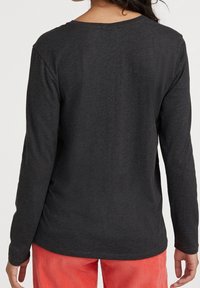 Schwarzes Langarmshirt aus weichem Stoff, mit einem runden Halsausschnitt und entspannter Passform, getragen zu leuchtend roten Cordhosen.