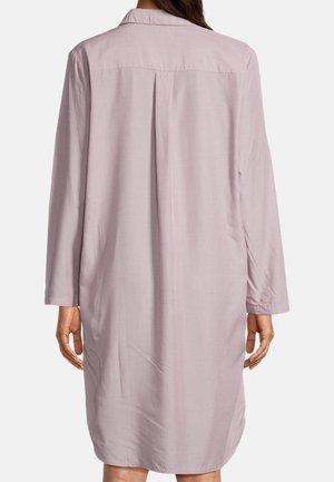 Kobieta ubrana w długą bluzkę z długim rękawem i jasnofioletową sukienkę do kolan, pokazana od tyłu na jednolitym tle.