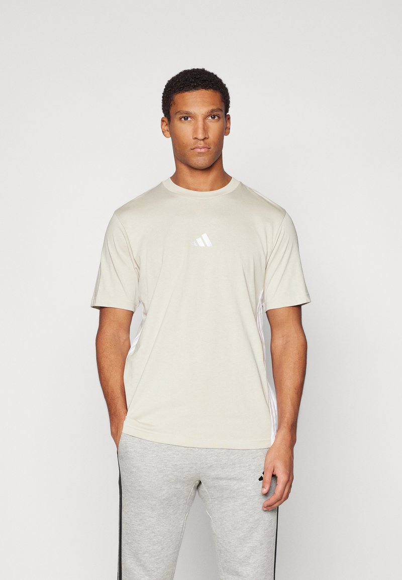 Beige Kurzarm-T-Shirt mit Rundhalsausschnitt und dezentem Dreistreifen-Design an den Seiten. Mit einem kleinen weißen Logo auf der Brust.