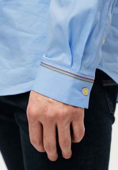 Φωτεινό γαλάζιο πουκάμισο με μανσέτα με κουμπάκι και πολύχρωμες ρίγες, με απαλό υφασμάτινο ύφασμα. Η μανσέτα ασφαλίζει με κίτρινο κουμπί.