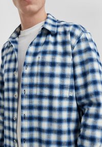 Blauwe en witte geruite flanellen shirt met knoopsluiting, kraag en een borstzak. Geweven stof met contrasterende patronen en stikdetails.