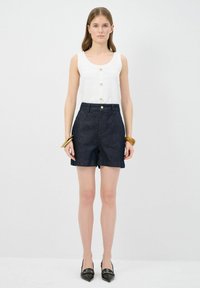 Vit ribbade linne med guldknappar, ihop med mörka denimshorts. Modellen bär svarta spetsiga skor och ett guldarmband.