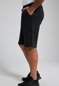 Schwarze Trainingsshorts aus strukturiertem Stoff, mit Seitentaschen und verstellbarem Bund, kombiniert mit schwarzen Sportschuhen.