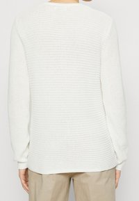 Pull en tricot blanc avec une coupe ample, une texture côtelée et des manches longues, avec des fentes sur les côtés à l'ourlet et un large décolleté.