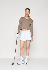 Καφέ κοντή μπλούζα v-neck, λευκή φούστα γκολφ, λευκά αθλητικά παπούτσια Nike και μπαστούνι γκολφ. Αξεσουάρ περιλαμβάνουν ένα γάντι και λευκές κάλτσες με λογότυπο.