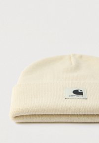 Πλεκτός σκούφος σε κρεμ απόχρωση με διπλωμένο ριμπ περιλαίμιο, διακοσμημένος με τετράγωνο λογότυπο Carhartt στο μπροστινό μέρος, με ανάγλυφη υφή.