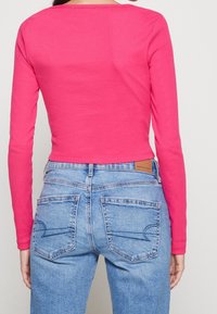 Dlouhý rukáv ve světlé růžové, v kombinaci se světle modrými džíny s vysokým pasem, které mají dvě zadní kapsy a koženou značkovouVisačku.