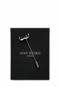 Metallnål i form av en mustasch, med en polerad silverfinish, fäst vid ett svart kort med "JOHN HENRIC" tryckt i silver.