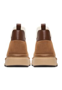 Un paio di stivali in suede beige per l'inverno con suole spesse beige, linguette del tallone in pelle marrone e rivestimento in pile bianco visibile nella parte superiore.