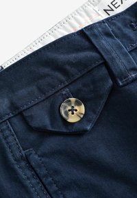 Pantalon en coton bleu marine avec une surface texturée, des détails de bouton jaune contrastant et une ceinture blanche avec un logo.
