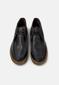 Schwarze Lederschuhe mit runder Spitze, Schnürdesign und einer strukturierten braunen Gummisohle. Sauberer, minimalistischer Stil ohne zusätzliche Verzierungen.