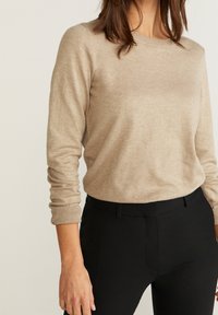 Beige Langarmpullover mit Rundhalsausschnitt, weicher Textur, gerippten Bündchen, kombiniert mit schwarzen, taillierten Hosen.