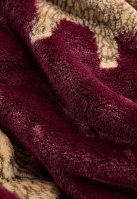 Plysset tæppe i dybe bordeaux- og beige nuancer med en blød, tekstureret overflade. Stoffet har en rig, fløjlsagtig fornemmelse og kontrasterende mønstre.
