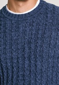 Marineblauer Strickpullover mit einem Zopfmuster, Rundhalsausschnitt und einer weichen Textur. Das Material scheint aus einem Wollgemisch zu bestehen.