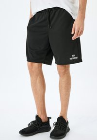 Sorte sports-shorts med elastisk talje og snor. Har sidelommer og "HIGH MOTIVATION" trykt i hvidt på kanten.