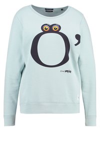 Lichtblauwe sweatshirt met lange mouwen, met een groot zwart "O" en een komma-ontwerp, kleurrijke ogen boven de "O" en kleine gedrukte tekst op de voorkant.